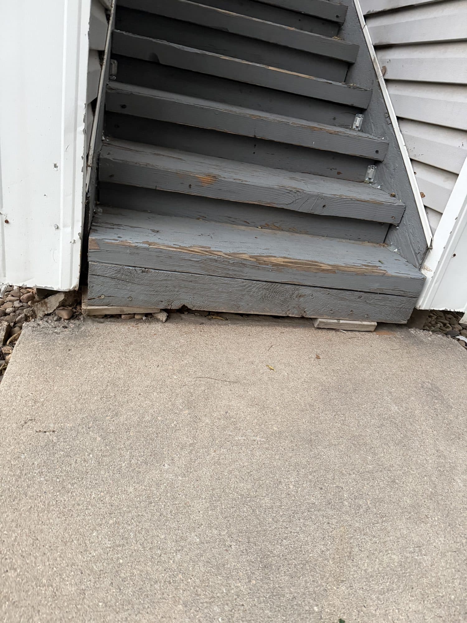Deteriorated wood stair base — IMG_1066: Rotting, split base of a wood stairway resting on a thin board rather than a proper footing, separating from the building.