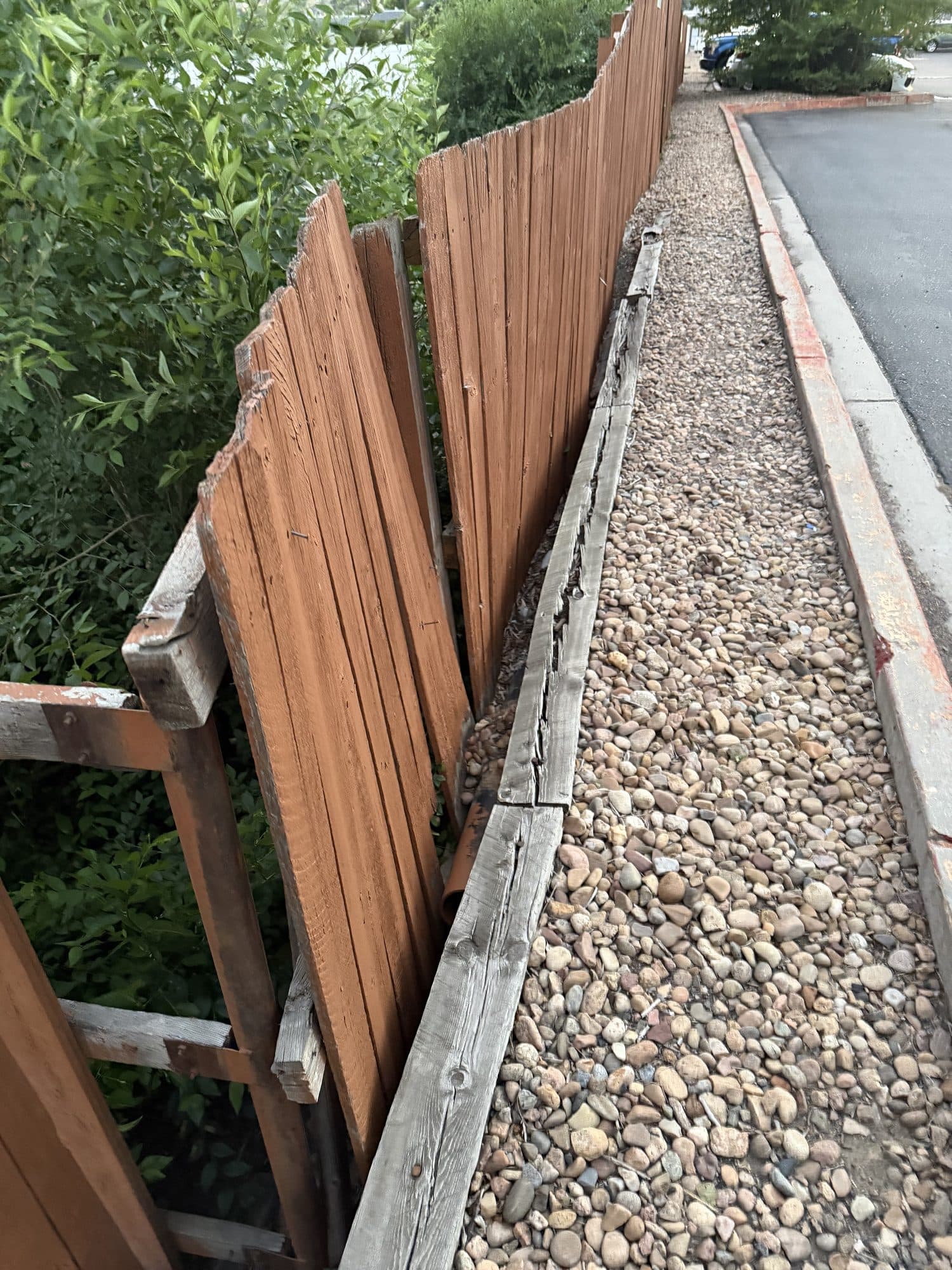 Broken wood fence section — IMG_1081: Broken/displaced section of a wood fence at a retaining curb.